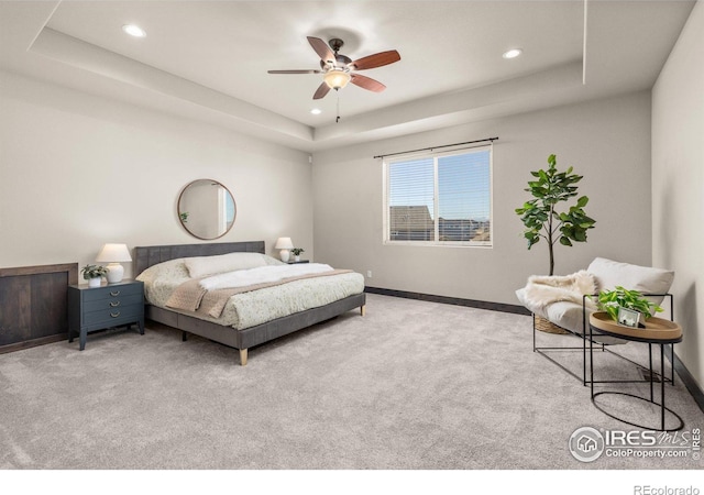 carpeted bedroom with ceiling fan and a tray ceiling