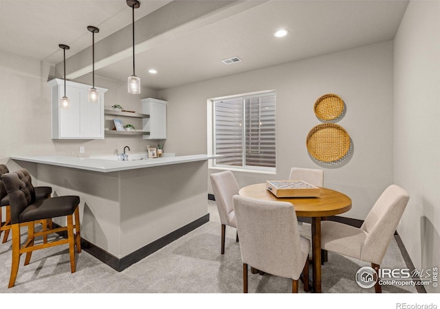 kitchen featuring white cabinetry, a kitchen bar, kitchen peninsula, decorative light fixtures, and light colored carpet