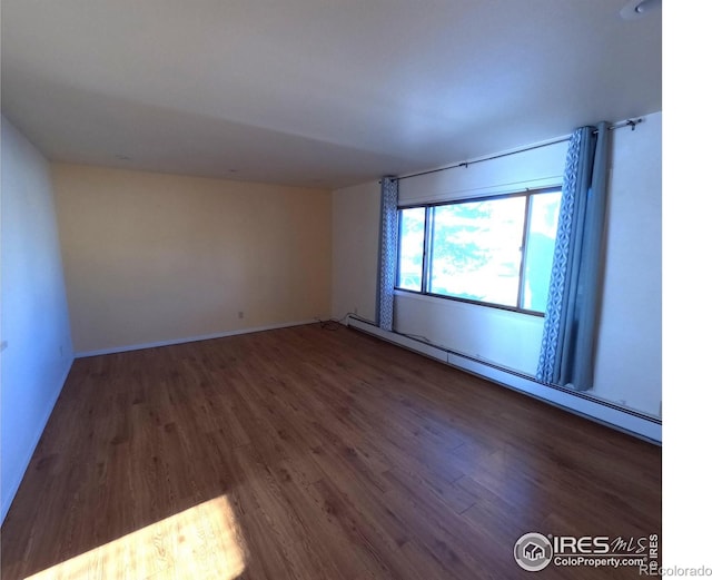 empty room featuring dark wood-type flooring and a baseboard radiator