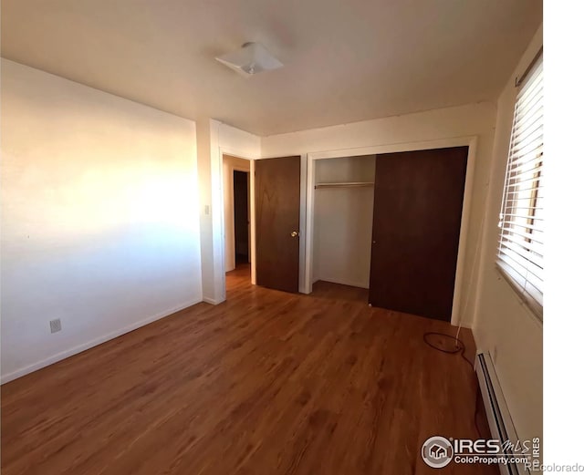 unfurnished bedroom with dark wood-type flooring, baseboard heating, and a closet