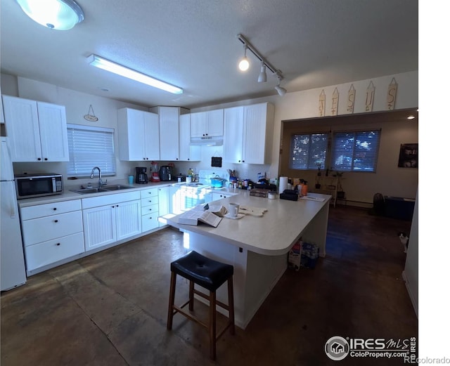 kitchen with a breakfast bar area, sink, white cabinets, and white appliances