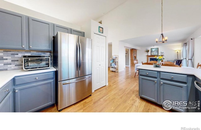 kitchen featuring an inviting chandelier, stainless steel fridge, decorative backsplash, light wood-type flooring, and pendant lighting