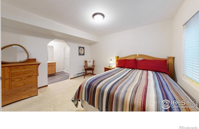 carpeted bedroom featuring a baseboard radiator, multiple windows, and ensuite bathroom