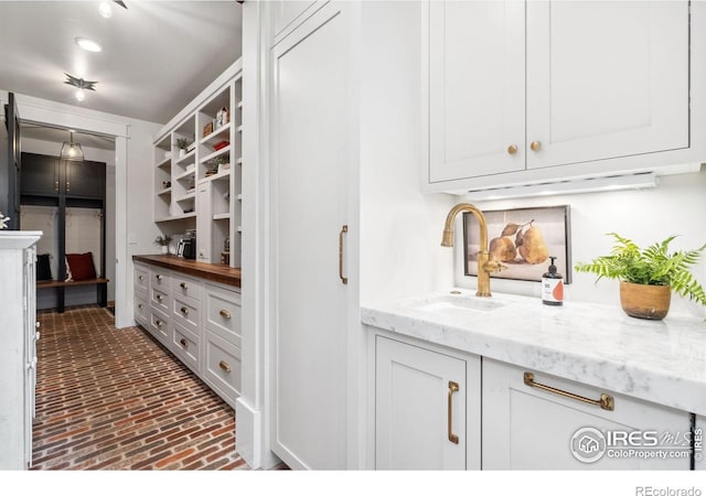 kitchen with a sink, open shelves, brick floor, and white cabinets