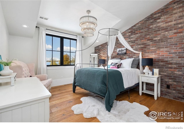 bedroom featuring visible vents, a notable chandelier, wood finished floors, brick wall, and lofted ceiling