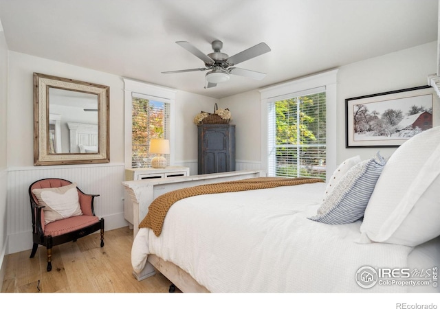 bedroom with wainscoting, light wood-type flooring, and ceiling fan