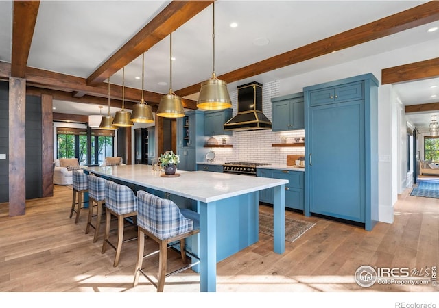 kitchen featuring a breakfast bar area, light wood-style flooring, blue cabinets, wall chimney exhaust hood, and tasteful backsplash