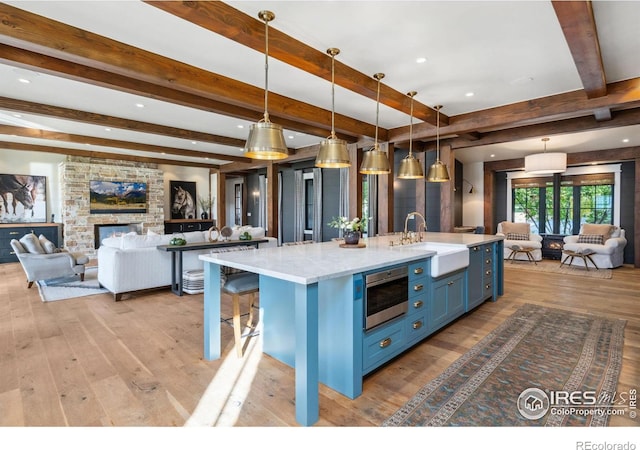 kitchen featuring blue cabinetry, a large island with sink, a sink, stainless steel microwave, and open floor plan