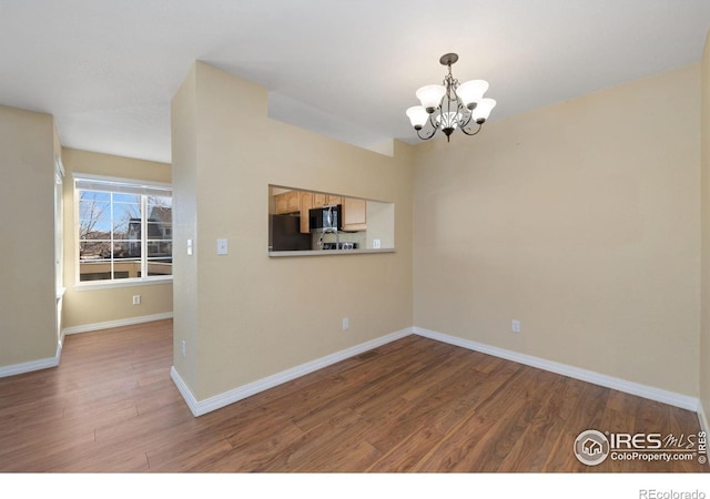 spare room featuring an inviting chandelier, baseboards, and wood finished floors