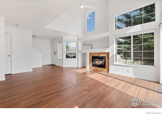 unfurnished living room featuring baseboards, a fireplace, wood finished floors, and a towering ceiling