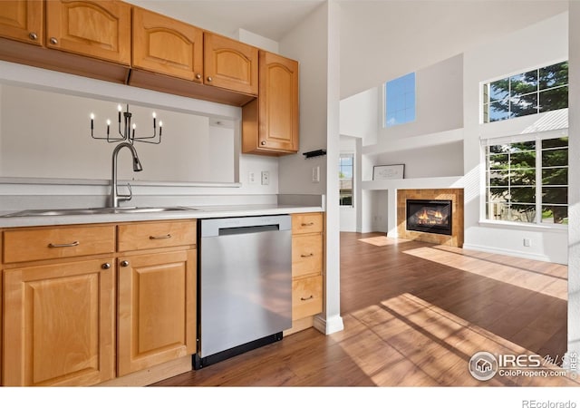kitchen featuring a towering ceiling, light countertops, a tile fireplace, a sink, and dishwasher