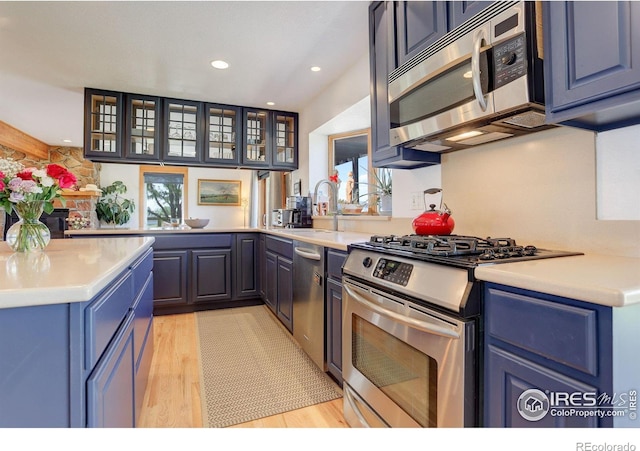 kitchen featuring light hardwood / wood-style floors, kitchen peninsula, sink, appliances with stainless steel finishes, and blue cabinets