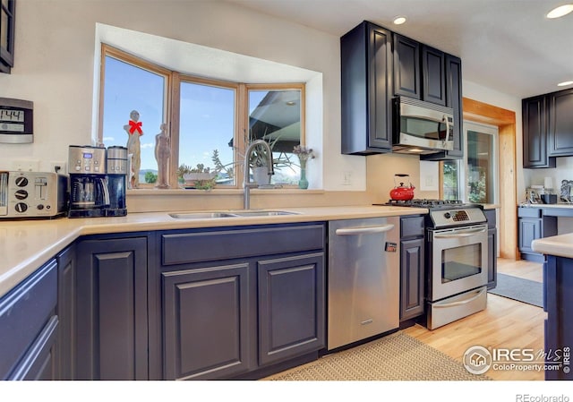 kitchen featuring light wood-type flooring, appliances with stainless steel finishes, a healthy amount of sunlight, and sink