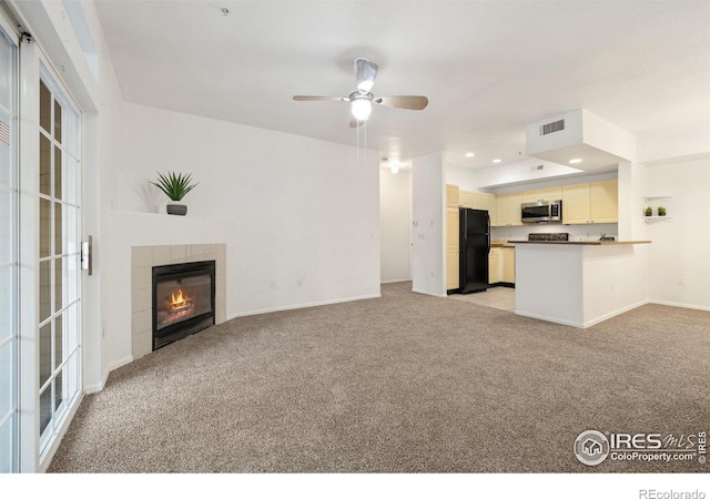 unfurnished living room featuring ceiling fan, light colored carpet, and a tile fireplace