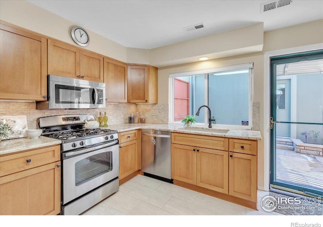 kitchen featuring appliances with stainless steel finishes, decorative backsplash, light stone counters, and sink