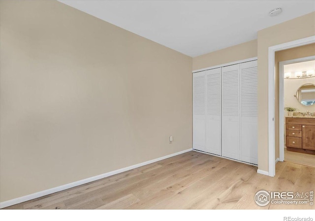 unfurnished bedroom with sink, ensuite bath, light hardwood / wood-style flooring, and a closet