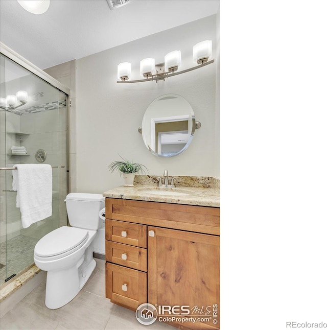 bathroom featuring toilet, vanity, tile patterned flooring, and a shower with door