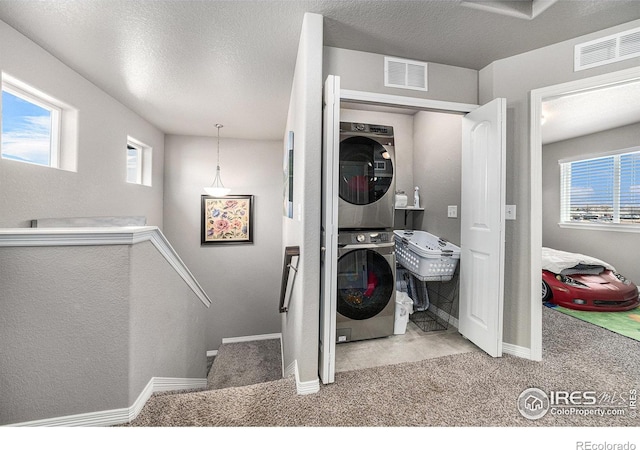 laundry area with light colored carpet, a wealth of natural light, stacked washer / drying machine, and a textured ceiling