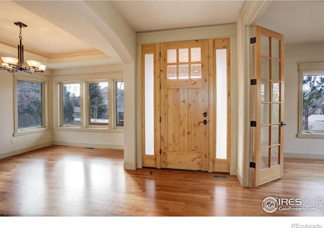 foyer entrance featuring light wood-type flooring, a raised ceiling, and an inviting chandelier