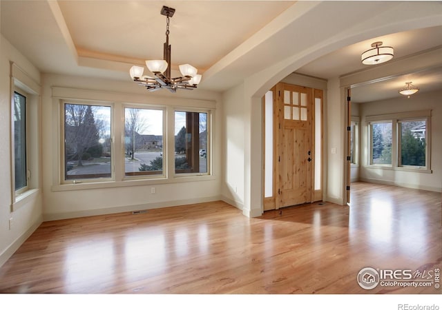 foyer entrance with light wood-type flooring, a notable chandelier, and a tray ceiling