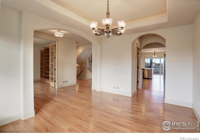 unfurnished room with light hardwood / wood-style floors, a tray ceiling, and an inviting chandelier