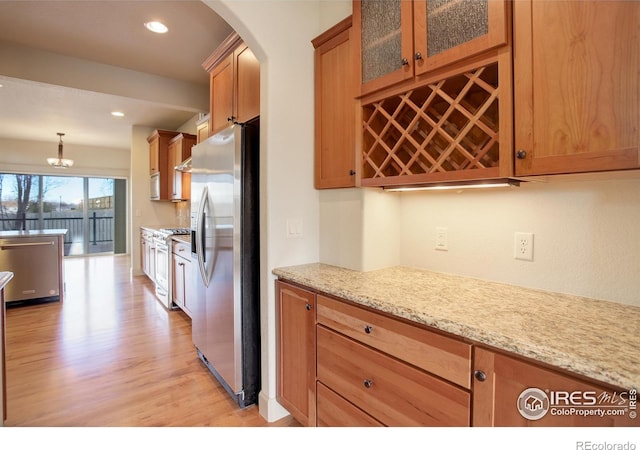 kitchen featuring decorative light fixtures, light stone countertops, stainless steel appliances, and light wood-type flooring