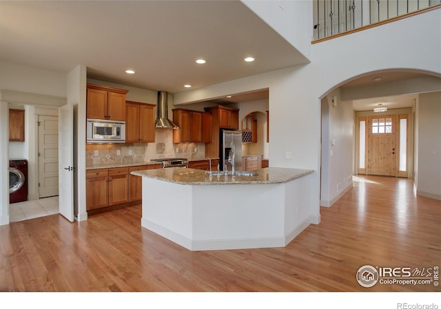 kitchen featuring stainless steel appliances, decorative backsplash, light stone countertops, washer / clothes dryer, and wall chimney range hood