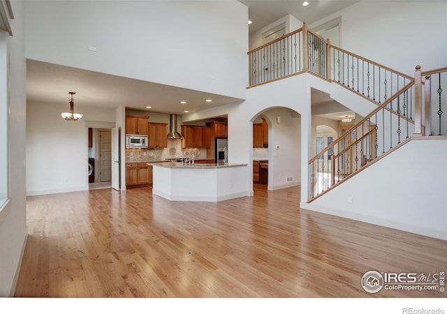 unfurnished living room with light hardwood / wood-style floors, a towering ceiling, and an inviting chandelier