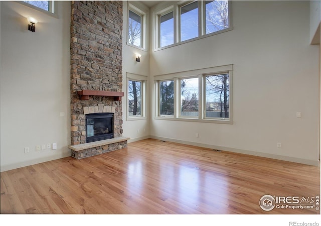 unfurnished living room featuring light hardwood / wood-style floors, a towering ceiling, and a fireplace