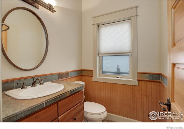 bathroom featuring toilet, vanity, and wooden walls