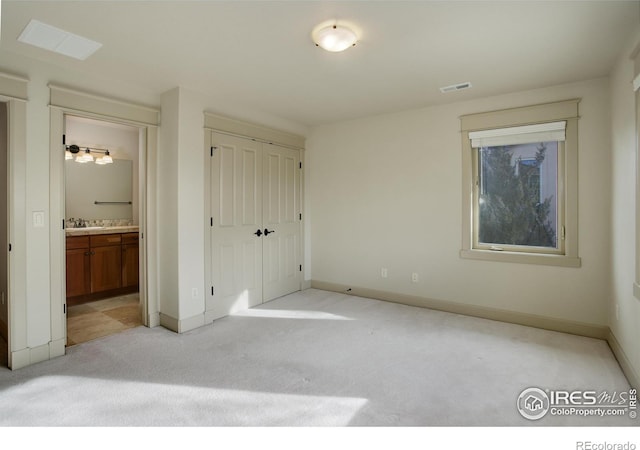 unfurnished bedroom featuring ensuite bathroom, a closet, and light carpet