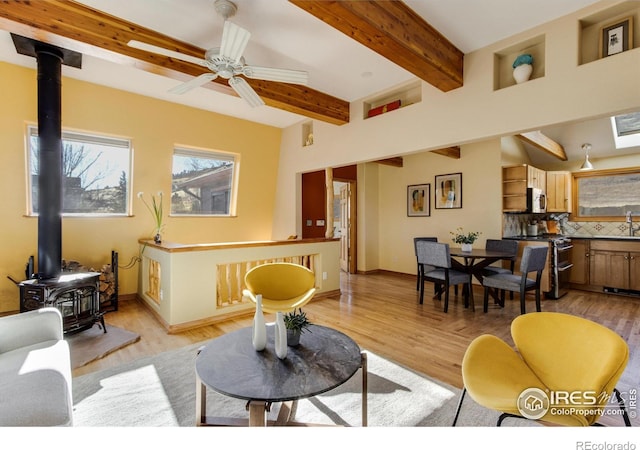 living room featuring ceiling fan, beam ceiling, a wood stove, and light hardwood / wood-style floors