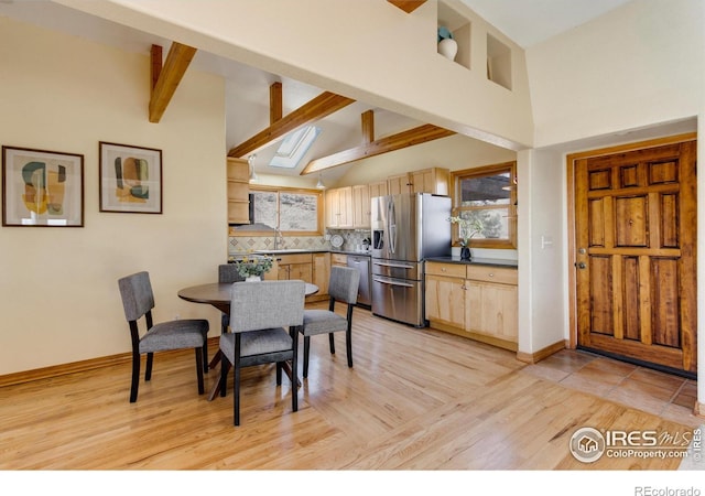 dining space featuring a skylight, light hardwood / wood-style floors, high vaulted ceiling, beam ceiling, and sink