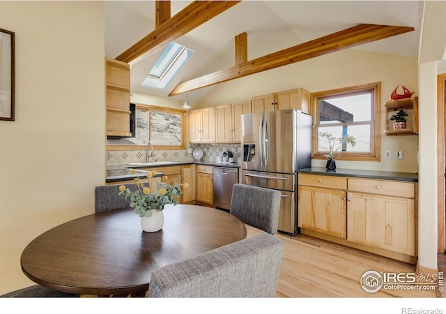 kitchen featuring lofted ceiling with skylight, appliances with stainless steel finishes, decorative backsplash, and light brown cabinets