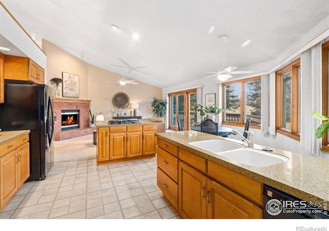 kitchen featuring black appliances, a fireplace, sink, vaulted ceiling, and light stone counters