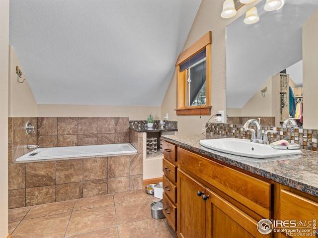 bathroom featuring a textured ceiling, tiled tub, tile patterned floors, vanity, and vaulted ceiling