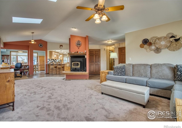 carpeted living room featuring lofted ceiling with skylight, ceiling fan, and a wood stove