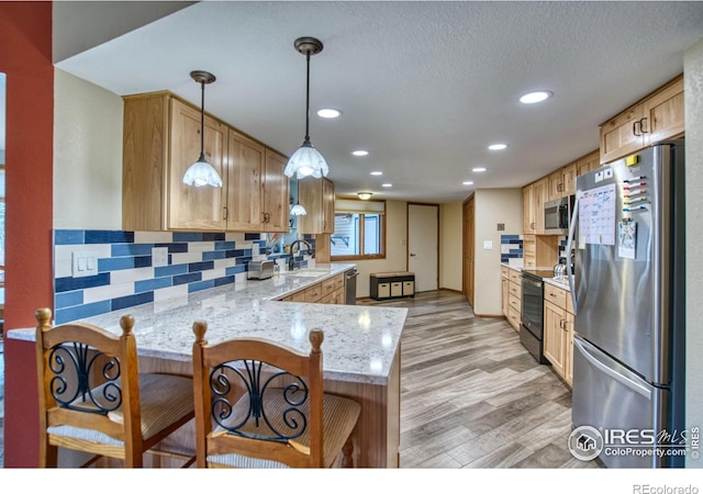 kitchen featuring sink, hanging light fixtures, stainless steel appliances, light stone countertops, and kitchen peninsula