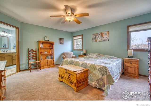 bedroom featuring ensuite bathroom, sink, light colored carpet, and ceiling fan