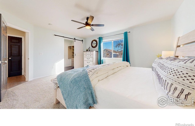 bedroom featuring light carpet, ceiling fan, a barn door, and a spacious closet