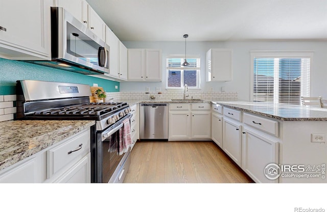 kitchen featuring pendant lighting, appliances with stainless steel finishes, white cabinetry, sink, and light stone counters