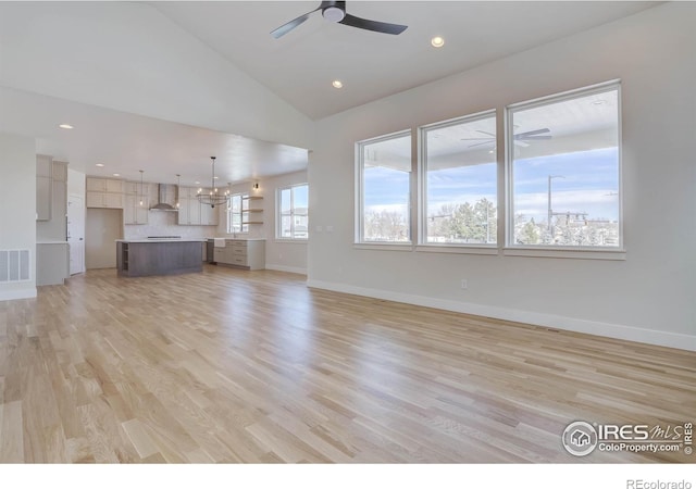 unfurnished living room featuring high vaulted ceiling, ceiling fan with notable chandelier, and light hardwood / wood-style floors