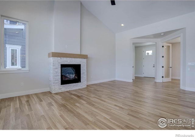 unfurnished living room featuring vaulted ceiling, a fireplace, and light hardwood / wood-style floors