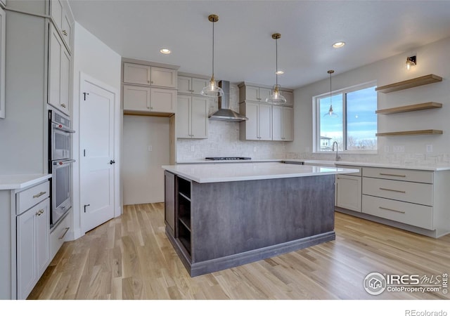 kitchen with gray cabinetry, backsplash, a center island, wall chimney exhaust hood, and light hardwood / wood-style flooring