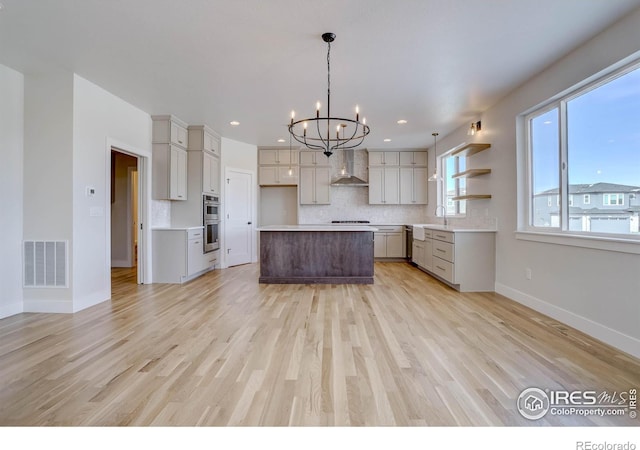 kitchen featuring a kitchen island, pendant lighting, gray cabinetry, wall chimney range hood, and light hardwood / wood-style flooring