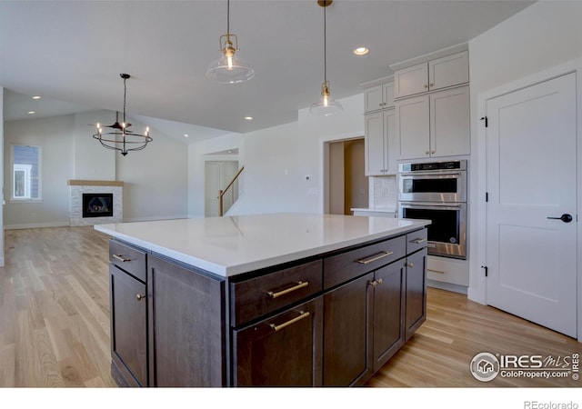 kitchen with hanging light fixtures, a center island, stainless steel double oven, and light hardwood / wood-style flooring