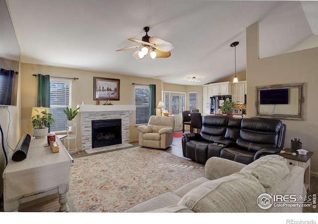 living room with ceiling fan, vaulted ceiling, and a fireplace