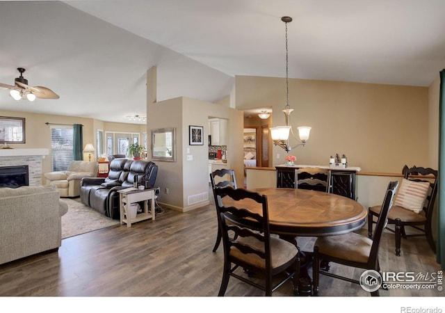 dining room with ceiling fan with notable chandelier, dark hardwood / wood-style flooring, lofted ceiling, and a fireplace