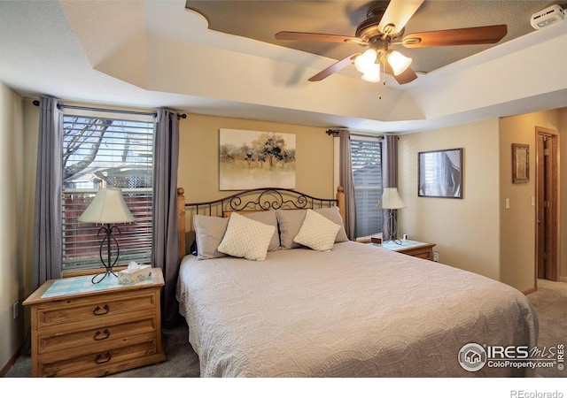 carpeted bedroom featuring ceiling fan and a raised ceiling