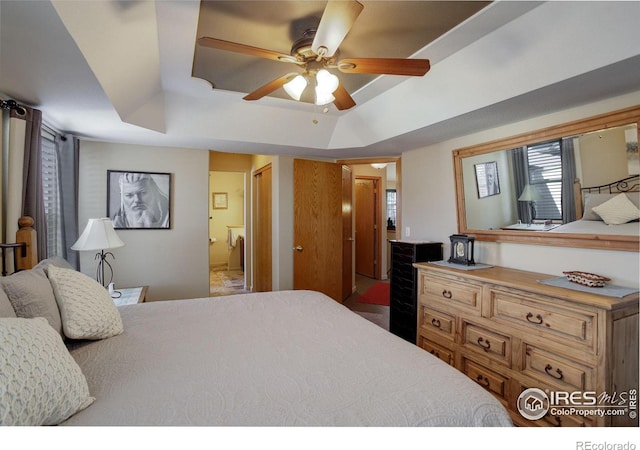 bedroom featuring ceiling fan, a tray ceiling, and ensuite bath